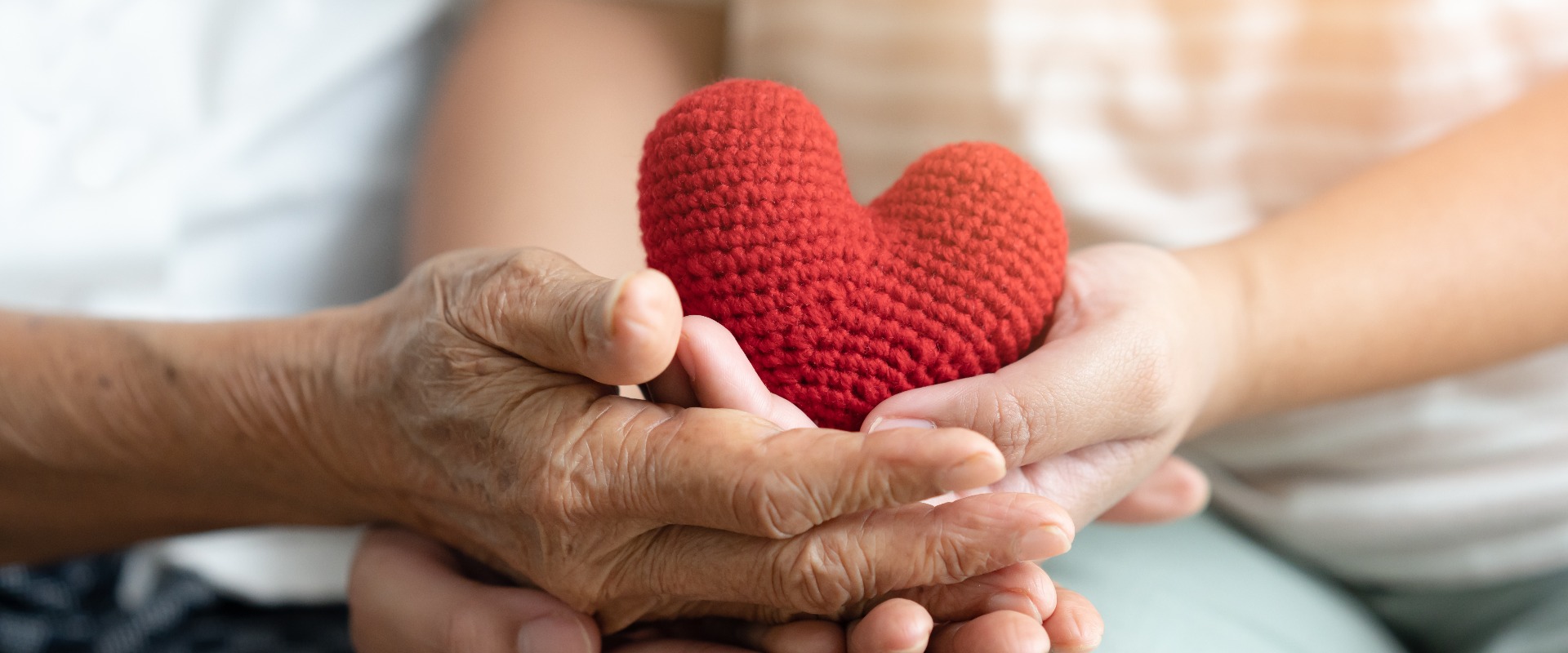 Young and senior woman holding each other hands and red yarn heart shape togetherness concept. Elderly care and protection with love from grandchild.