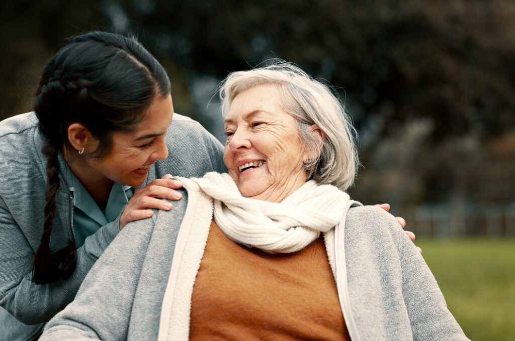 Pflegerin hilft behinderter Frau im Park für Unterstützung, Vertrauen und Pflege im Ruhestand. Krankenschwester im Gespräch mit einem glücklichen älteren Patienten im Rollstuhl für Rehabilitation, Therapie und Konversation im Garten
